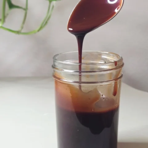 Homemade Chocolate syrup in a mason jar with chocolate syrup dripping off the spoon