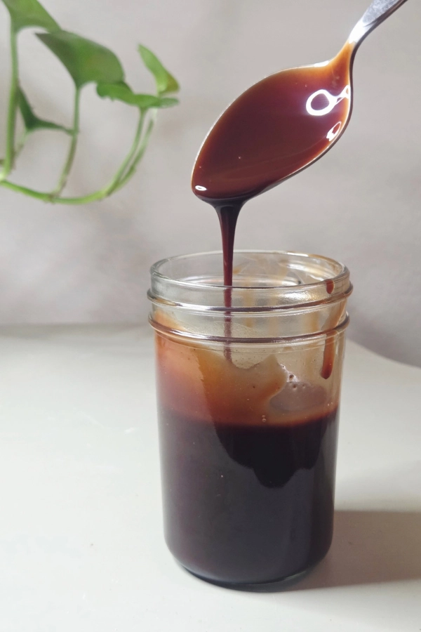 Homemade Chocolate syrup in a mason jar with chocolate syrup dripping off the spoon