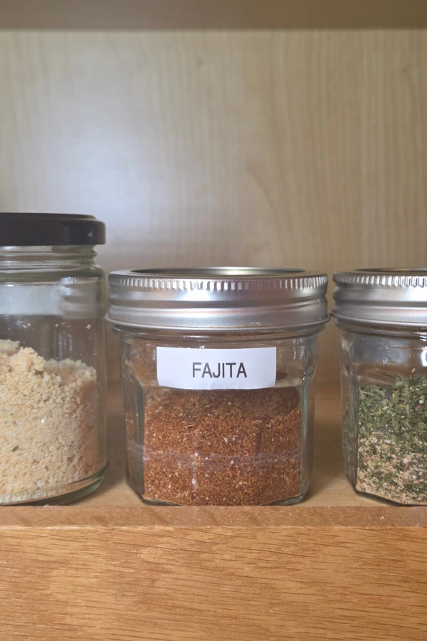 homemade fajita seasoning in a labeled glass jar on a wood pantry shelf