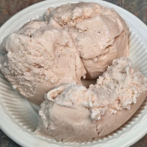 Overhead view of homemade strawberry ice cream scoops in a white ribbed bowl