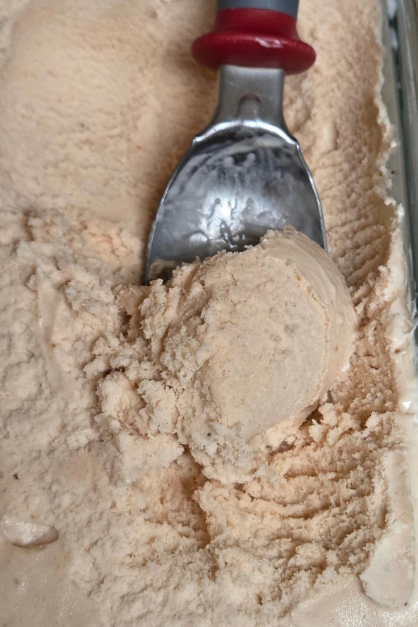 Close up of a scoop of homemade strawberry ice cream being lifted from a glass pan