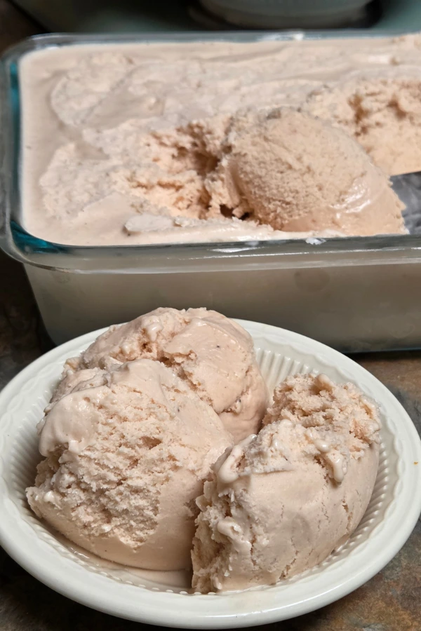 Bowl of homemade strawberry ice cream scoops with glass loaf pan in background
